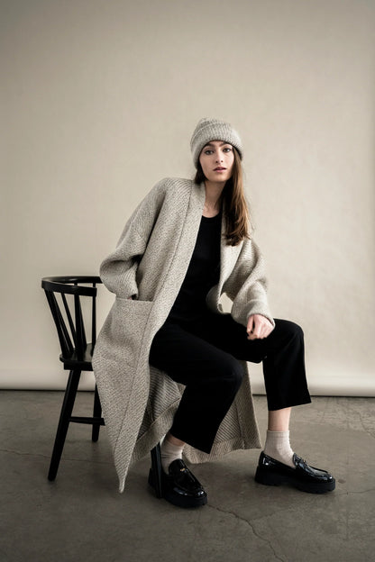 BodyBag by Jude long textured beige cardigan with pockets worn over black outfit and beanie while seated in Kelowna