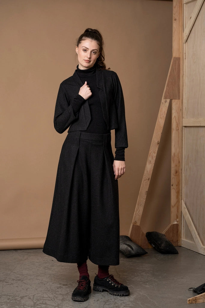 Woman holding the front edge of the Bodybag by Jude Nassau Jacket in Charcoal, showing the open front and the brushed wool blend texture.