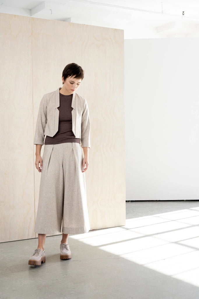 Woman looking down in the Bodybag by Jude Nassau Jacket in Sand, showing the notched front edges and the soft oatmeal wool blend.