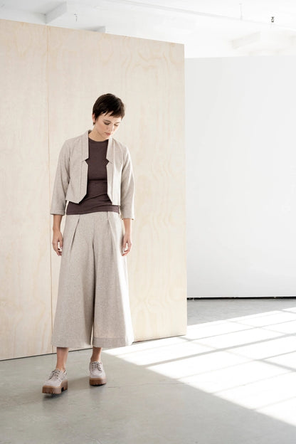 Woman looking down in the Bodybag by Jude Nassau Jacket in Sand, showing the notched front edges and the soft oatmeal wool blend.