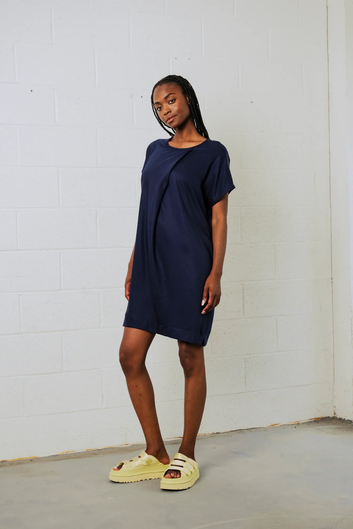 Woman wearing a navy blue dress standing against a white brick wall.