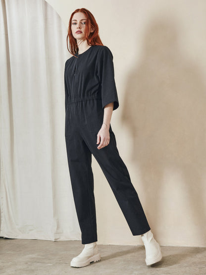 Woman wearing a black jumpsuit standing against a neutral background
