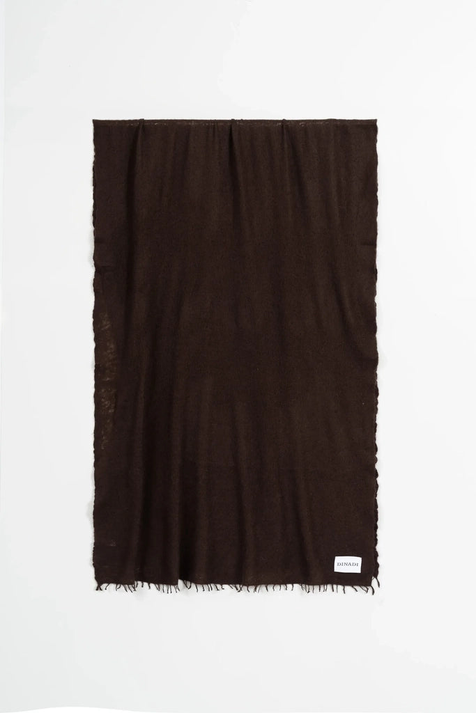 A dark brown rectangular scarf with fringed edges, displayed flat against a clean white background. A small white brand tag is visible in the bottom right corner.