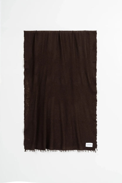 A dark brown rectangular scarf with fringed edges, displayed flat against a clean white background. A small white brand tag is visible in the bottom right corner.