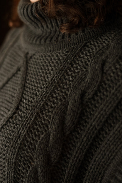 Close-up of a dark charcoal gray cable-knit turtleneck sweater dress, showing the detailed knit texture and ribbed collar.