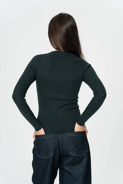Person wearing a dark green long-sleeve top and dark jeans on a white background