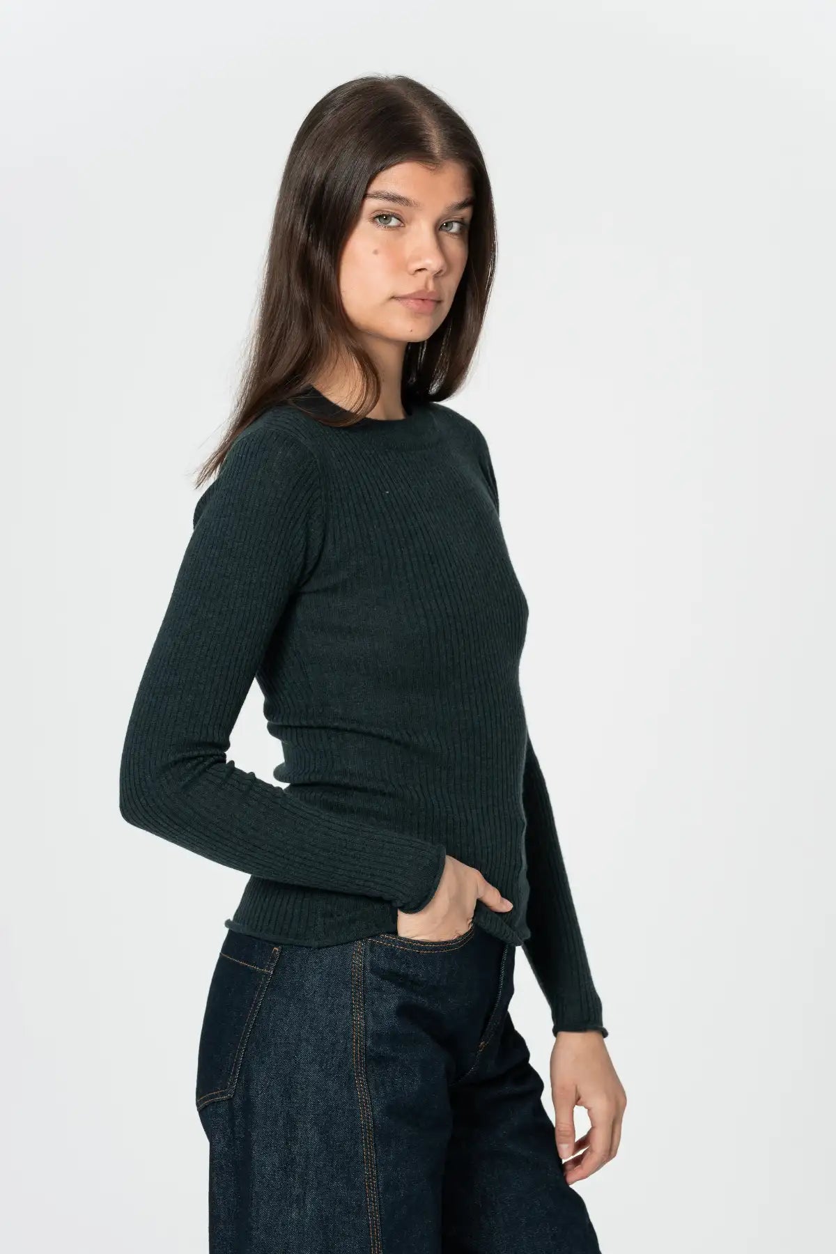 Woman wearing a dark green sweater and jeans on a white background