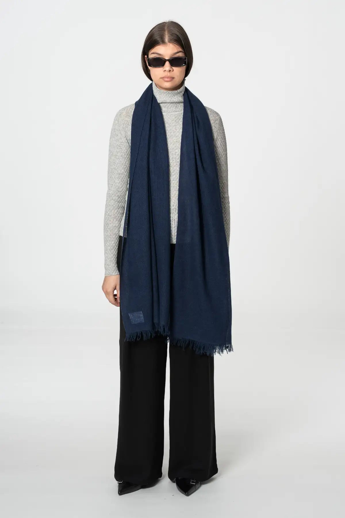 Person wearing a navy scarf, gray sweater, and black pants on a white background
