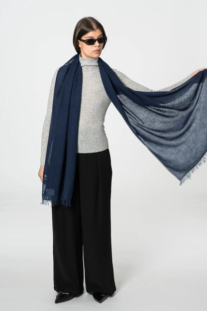 Woman wearing a navy blue scarf, gray sweater, and black pants on a white background