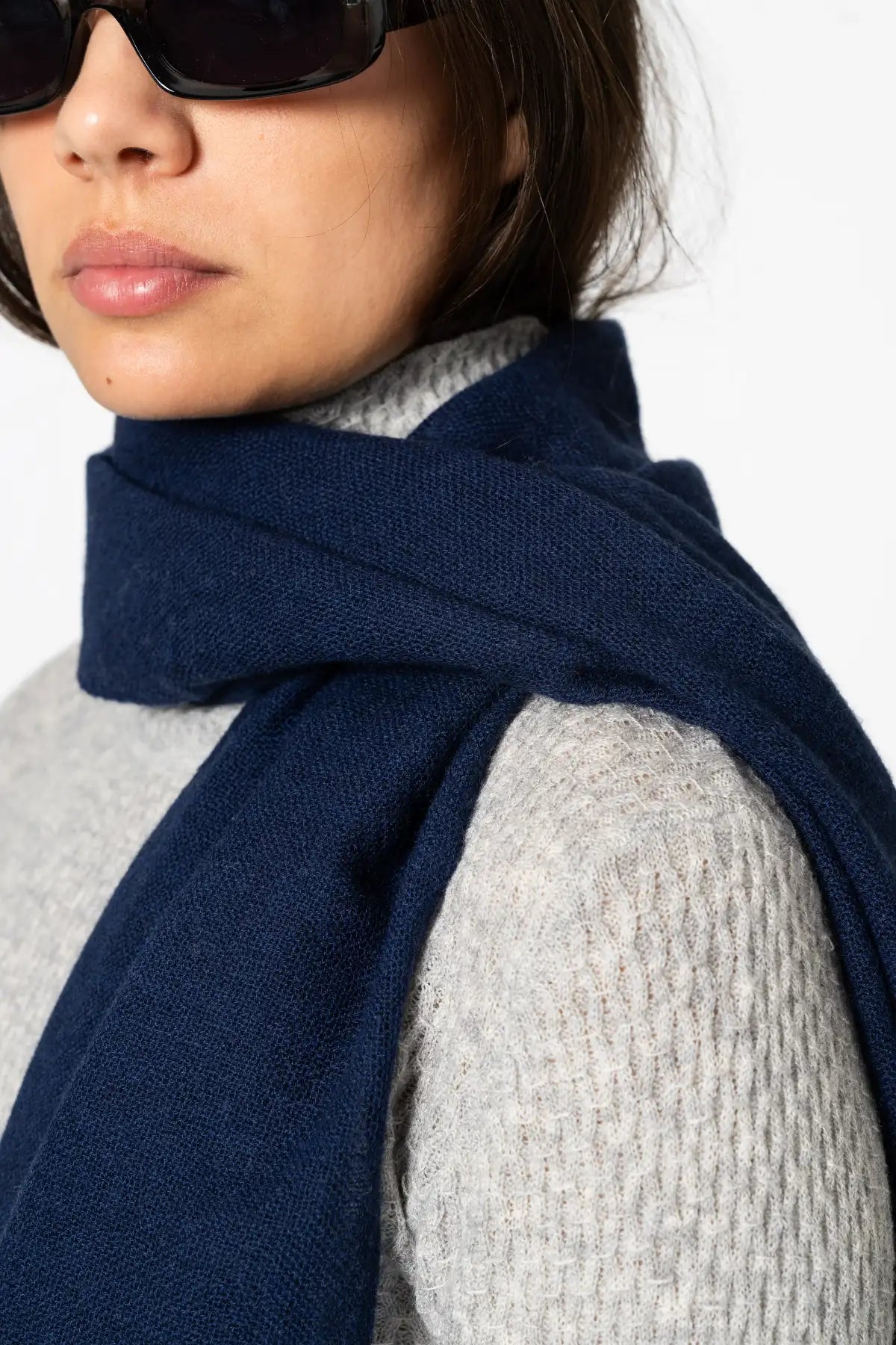 Person wearing a navy blue scarf and sunglasses on a white background