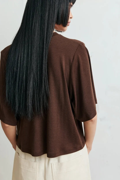 A person shown from the back wearing a brown short-sleeve top and cream-colored pants against a light gray background.