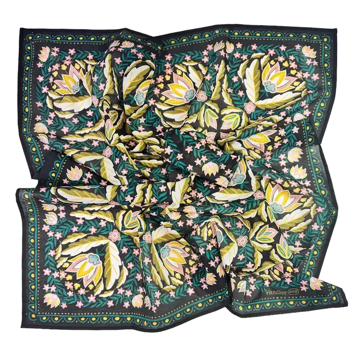 A square silk scarf featuring a botanical pattern with large yellow and green leaves, pink flowers, and a dark border, laid flat on a white background.