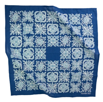 A square blue scarf with a repeating white and light blue floral and geometric tile pattern, laid flat against a white background.