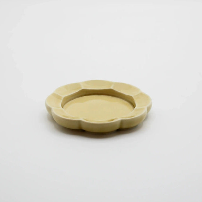 A small, scalloped ceramic dish in a pale yellowish-beige color, photographed from a top-down perspective on a clean white background.