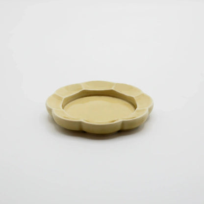 A small, scalloped ceramic dish in a pale yellowish-beige color, photographed from a top-down perspective on a clean white background.