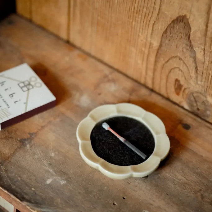 a cream-coloured ceramic flower-shaped incense tray holding a hibi 10minutes aroma incense match