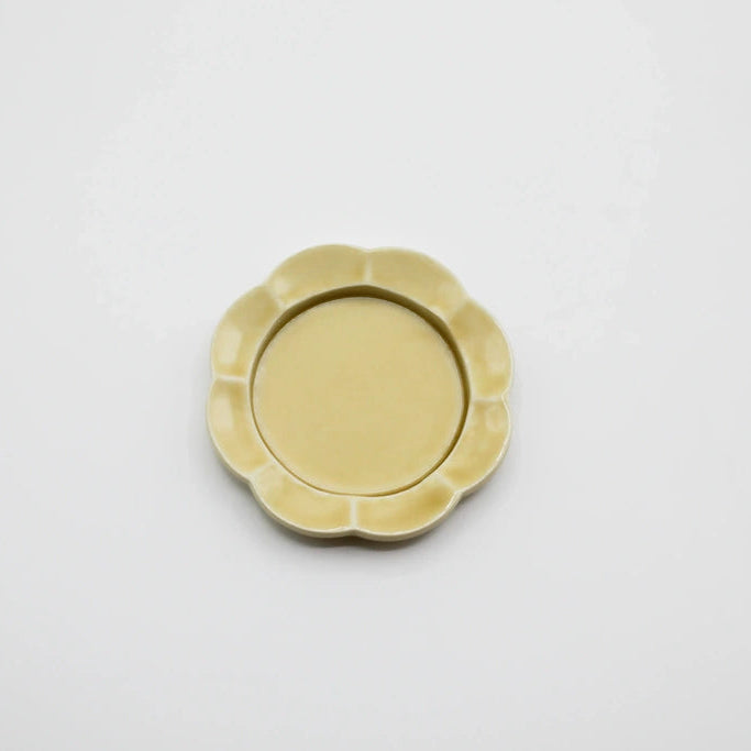 A small round ceramic dish with a scalloped flower-like rim, shown from above on a plain white background.