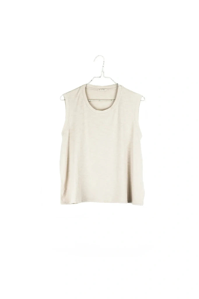 A sleeveless, scoop-neck knit top in a light cream or off-white color, hanging on a white plastic hanger against a solid white background.