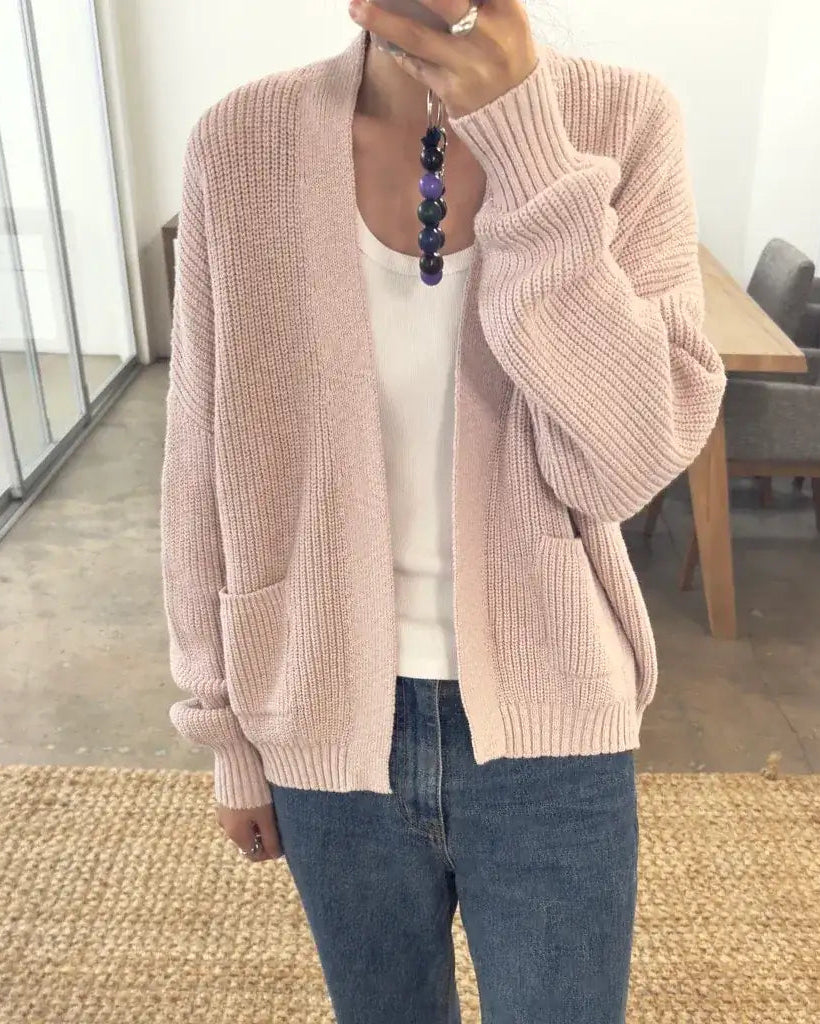 Person wearing a pink cardigan over a white shirt and blue jeans indoors.