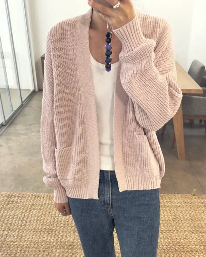 Person wearing a pink cardigan over a white shirt and blue jeans indoors.