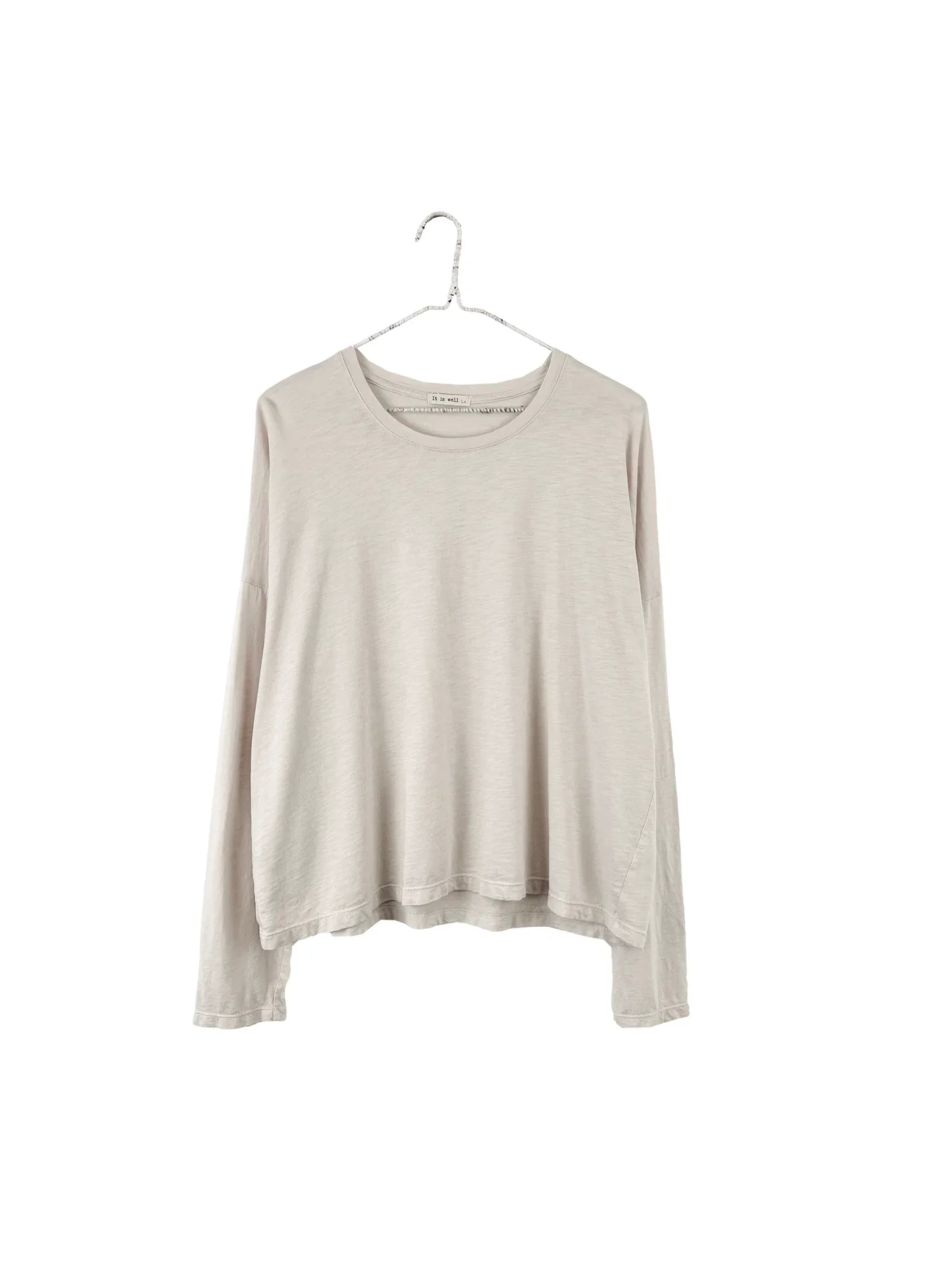 A light beige long-sleeve knit top hanging on a metal hanger against a plain white background.