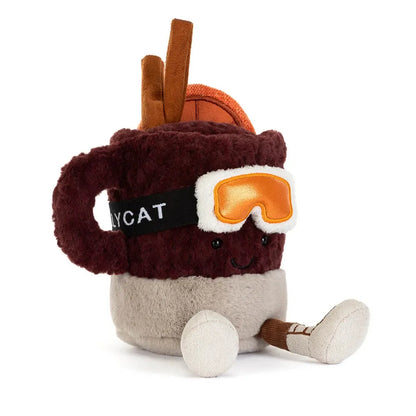 A plush toy shaped like a mug with a smiling face, wearing orange goggles and brown boots, on a solid white background.