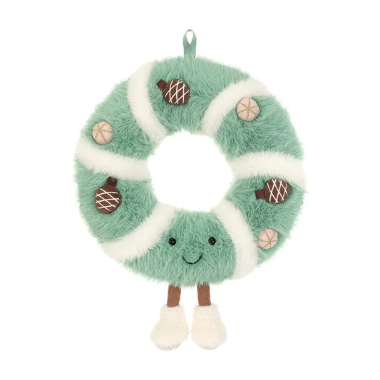 Front view of the Jellycat Amuseables Pinecone Wreath, a fluffy sage green plush wreath wrapped in cream swirls, with brown pinecones, pink baubles, a smiling face and cream boots on little legs, on a white background.