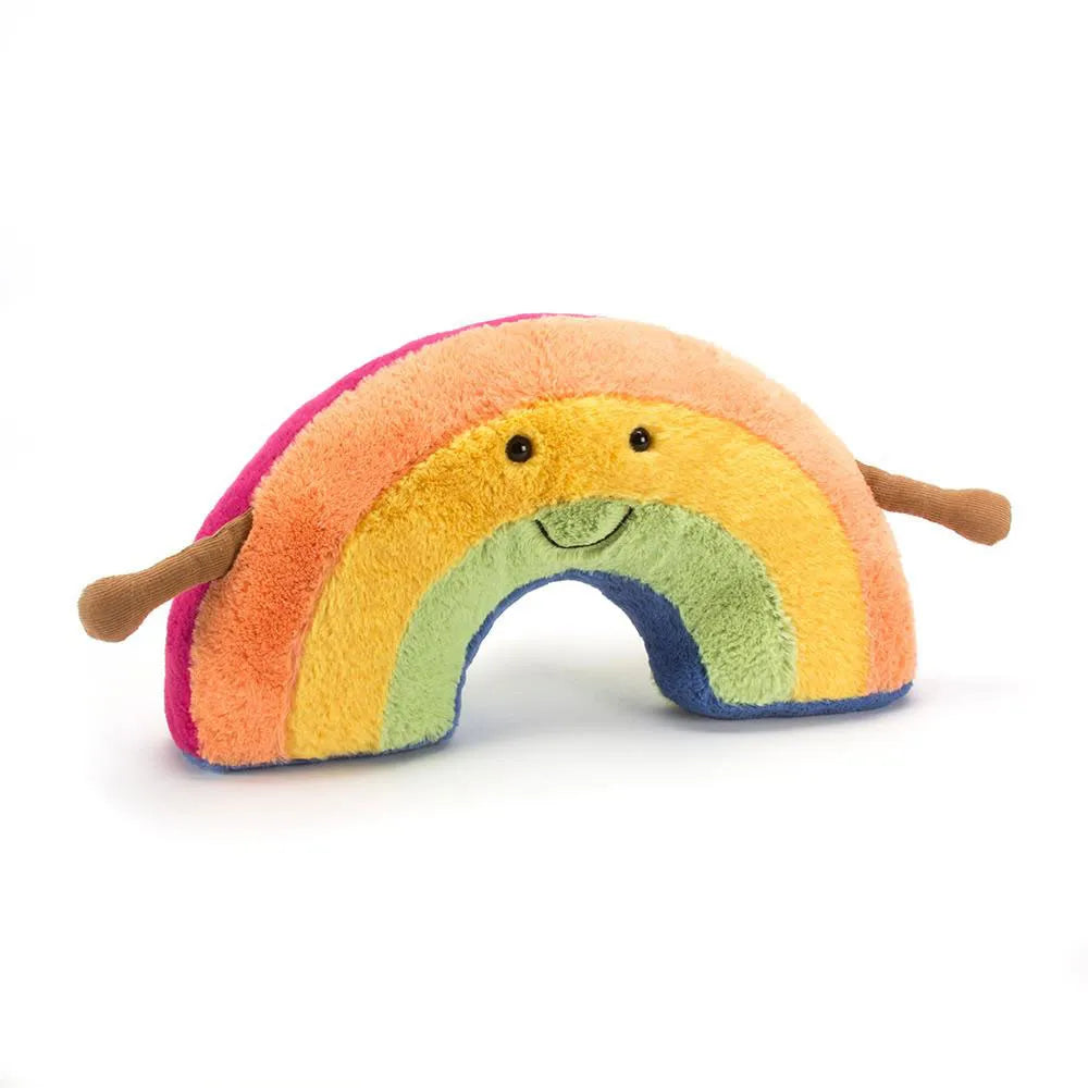 A plush rainbow toy with a smiling face, featuring soft fuzzy stripes in pink, orange, yellow, green, blue, and purple, with small brown arms, photographed on a clean white background.