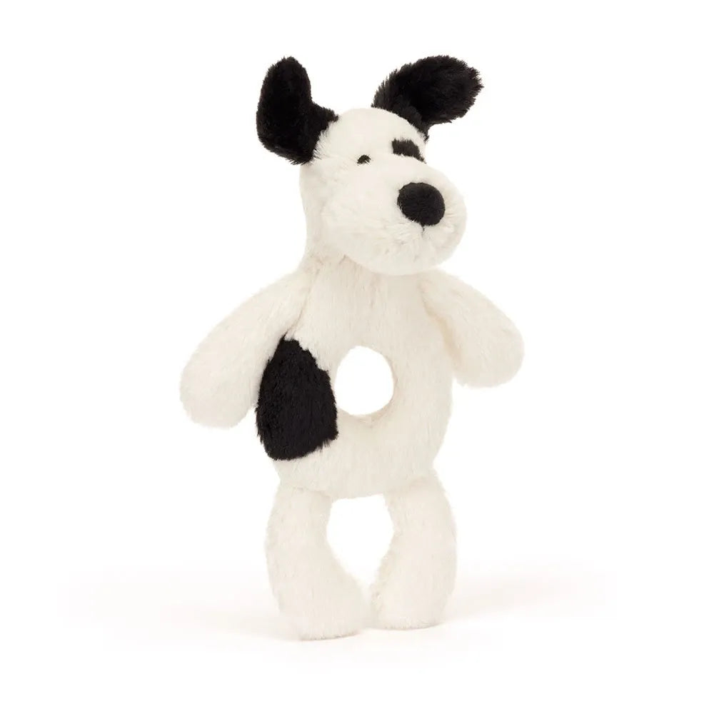 A plush dog rattle toy with a white body, black ears, black nose, and a black patch on its back, featuring a circular hole in the center for hanging or cradling.