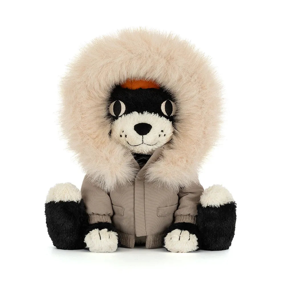 Front view of Jellycat Jack Alpine sitting upright, peeking out from a fluffy cream fur-trimmed hood, in a taupe parka with pockets and ribbed cuffs, with black and cream paws.