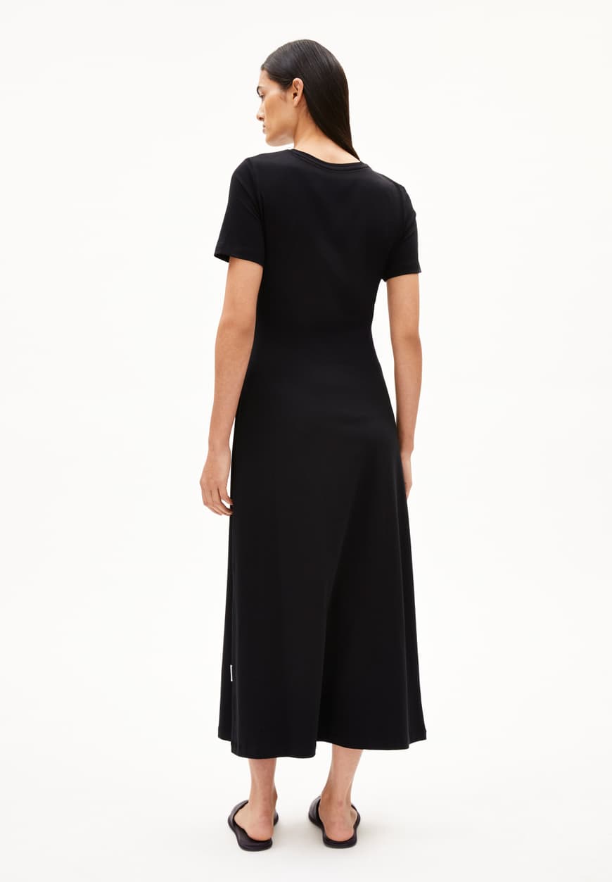 BACKSIDE OF BLACK SHEATH WRAP DRESS ON MODEL WITH BLACK HAIR AND FLAT SANDALS AGAINST WHITE BACKGROUND