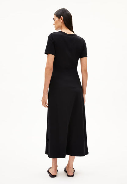 BACKSIDE OF BLACK SHEATH WRAP DRESS ON MODEL WITH BLACK HAIR AND FLAT SANDALS AGAINST WHITE BACKGROUND