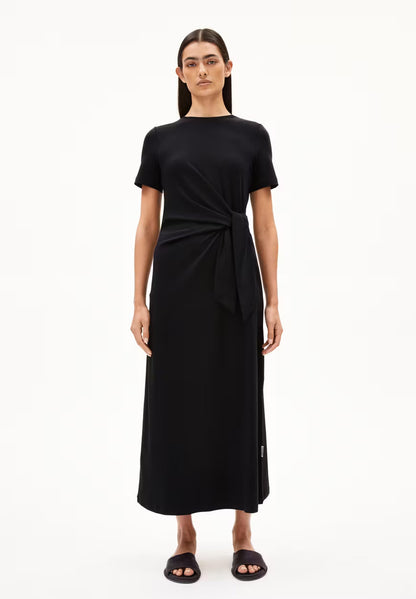 BLACK SHEATH WRAP DRESS ON MODEL WITH BLACK HAIR AND FLAT SANDALS AGAINST WHITE BACKGROUND