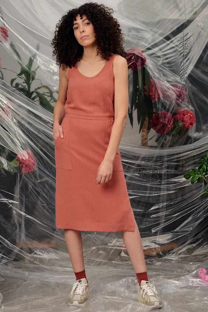 Woman in the Jennifer Glasgow Design Aisha Dress in Terracotta, styled with red socks and trainers, in front of draped clear plastic and red flowers.