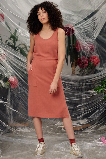 Woman in the Jennifer Glasgow Design Aisha Dress in Terracotta, styled with red socks and trainers, in front of draped clear plastic and red flowers.