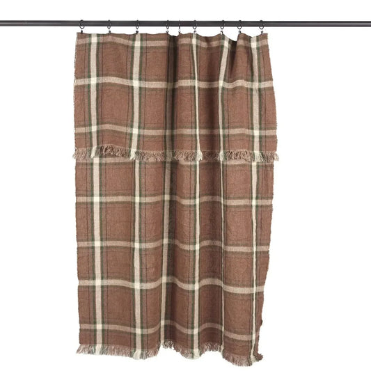 The Libeco Pièce de Lin in Rowan Check hanging from a black curtain rod with ring clips and a folded-over top, showing the chestnut brown linen with a cream and green check and loose fringed edges.