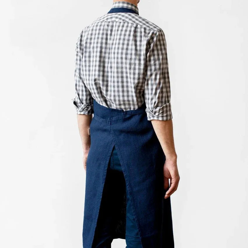 A man shown from the back wearing a dark navy apron over a black and white gingham check shirt, set against a plain white studio background.