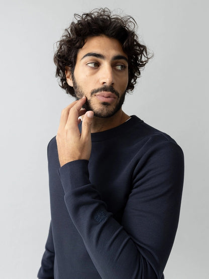 Close-up of a man looking to the side in the MOS MOSH Gallery Canada Abel Crew Neck Sweat in salute navy melange, showing the ribbed crew neck, against a light grey background.