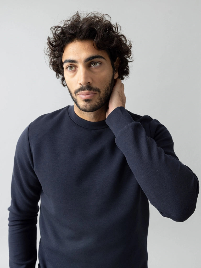 Man with one hand on his neck wearing the MOS MOSH Gallery Canada Abel Crew Neck Sweat in salute navy melange, against a light grey studio background.
