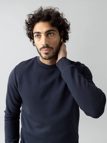 Man with one hand on his neck wearing the MOS MOSH Gallery Canada Abel Crew Neck Sweat in salute navy melange, against a light grey studio background.