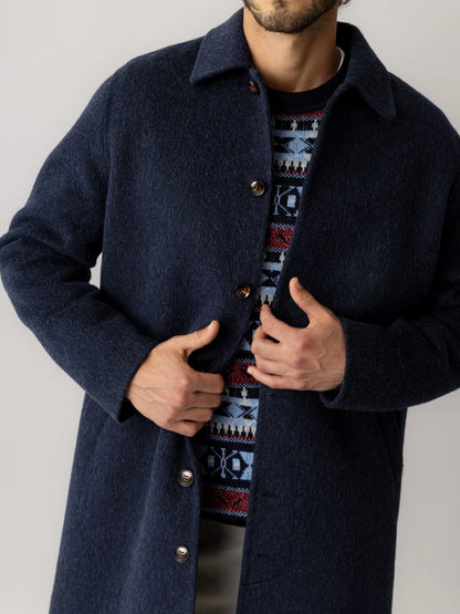 Close-up of a man fastening the tortoiseshell-style buttons on the MOS MOSH Gallery Canada Barkley Wool Coat in salute navy, showing the brushed wool texture over a patterned knit.