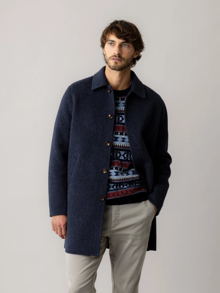 Man wearing the MOS MOSH Gallery Canada Barkley Wool Coat in salute navy over a patterned knit with light grey chinos, hands in pockets, against a light grey studio background.