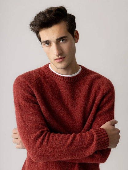 Man with crossed arms wearing the MOS MOSH Gallery Canada Carlos Crew Neck Knit in burnt russet over a white tee, against a light grey studio background.