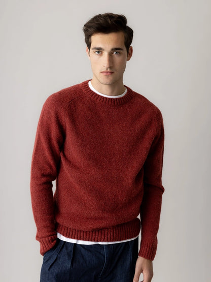 Man wearing the MOS MOSH Gallery Canada Carlos Crew Neck Knit in burnt russet over a white tee with dark denim trousers, against a light grey studio background.