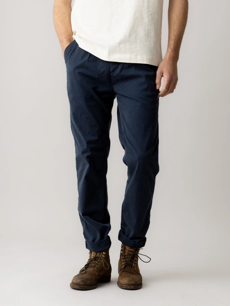 Close-up of a man wearing the MOS MOSH Gallery Canada Jones All-Day Pant in Salute Navy, showing the pleated front, side pocket and cuffed hem with brown boots.
