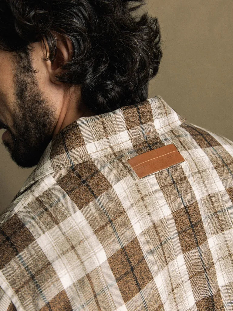Close-up of the back collar of the MOS MOSH Gallery Canada Trossard Jacket in toffee check, showing the leather-look brand patch, against a warm beige backdrop.