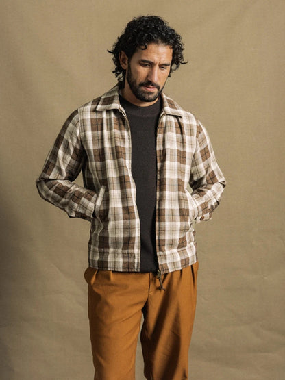 Man wearing the MOS MOSH Gallery Canada Trossard Jacket in toffee check, open over a dark knit with rust trousers, against a warm beige backdrop.