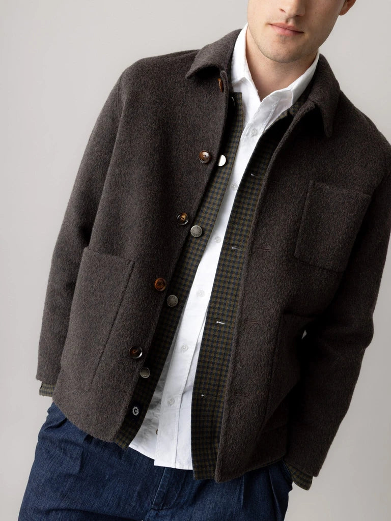 Close-up of a man wearing the MOS MOSH Gallery Canada Warren Jacket in delicioso brown, showing the patch pockets and buttons over a check overshirt, against a light grey studio background.