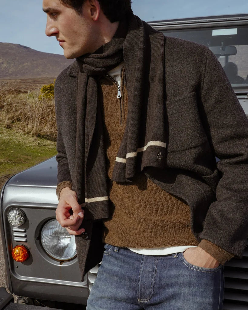 Man looking to the side wearing the MOS MOSH Gallery Canada Warren Jacket in delicioso brown with a brown scarf and quarter-zip knit, standing by a vintage off-road vehicle in the hills.