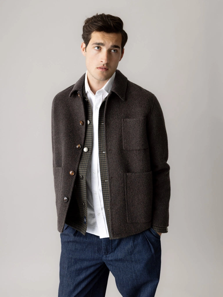 Man wearing the MOS MOSH Gallery Canada Warren Jacket in delicioso brown, open over a check overshirt and white shirt with dark denim trousers, against a light grey studio background.